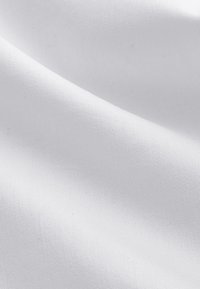 Gros plan d'un tissu blanc lisse avec un pli diagonal subtil montrant une texture fine et un motif de tissage.