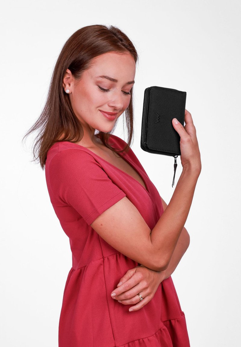 Black zippered wallet with a textured surface, held in a hand. A person in a rose-colored dress poses against a white background.