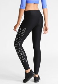 Leggings neri con la scritta "JUST DO IT." stampata in bianco sul lato sinistro. Indossati con un top corto blu e scarpe da ginnastica nere.