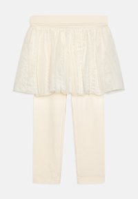 Leggings de couleur crème avec une jupe en tulle superposée, dotées d'une taille douce et d'une texture lisse. L'ensemble est simple et élégant.
