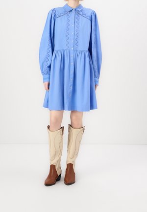 Light blue long-sleeve button-down dress with embroidered details, paired with beige and brown knee-high western-style boots.