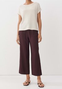 Ljust beige kortärmad stickad topp kombinerad med lösa, mörk burgundy vida byxor. Svarta flip-flop-sandaler fulländar outfiten med en enkel design.