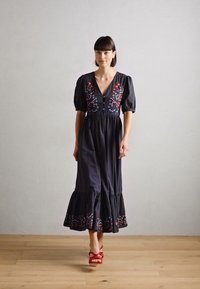 Schwarzes Baumwollkleid mit Puffärmeln, V-Ausschnitt, gestickten floralen Details in Rot und Blau sowie einem gestuften Rüsche am Saum.