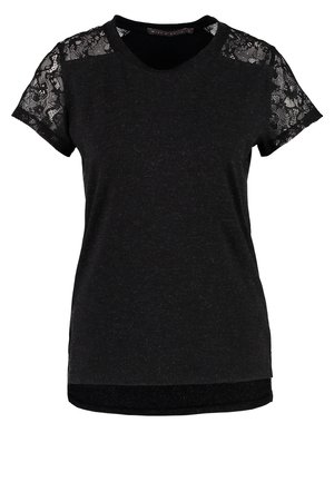 Mujer caminando, lleva una blusa negra con mangas de encaje, falda blanca, medias negras, zapatos negros puntiagudos y lleva un bolso negro grande.