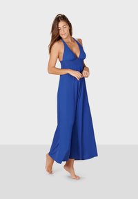 Blå halterneck-klänning med djup V-ringning, flödande hellång kjol, tillverkad av mjukt tyg, med en åtsittande överdel och lös underdel.