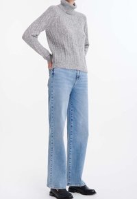 Szary prążkowany sweter z golfem zestawiony z jasnoniebieskimi spodnimi o szerokich nogawkach oraz czarnymi butami. Sweter ma wysoki kołnierz i teksturowaną tkaninę.