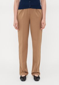 Tan pantalon met een rechte pasvorm, voorplooien en zijzakken, gecombineerd met zwarte instappers.