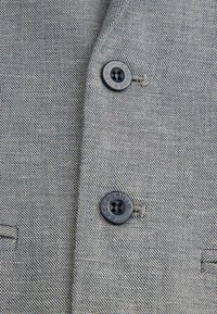 Tkanina żakietu w szaro-czarny wzór w zębatkę, z dwoma czarnymi guzikami i subtelnymi detalami szycia w pobliżu guzików.