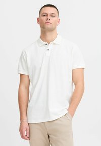 Hvid polo t-shirt med korte ærmer, med en klassisk krave og to-knaps placket. Indhold af marineblå knapper og et blødt, struktureret stof.