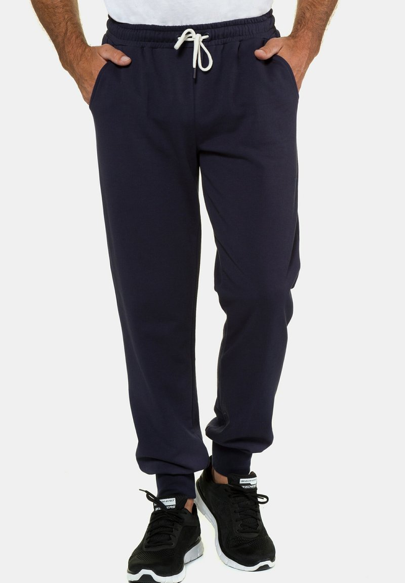 Navy Sweatpants mit elastischem Bund und Kordelzug; ausgestattet mit zwei Seitentaschen und gerippten Bündchen. Kombiniert mit schwarzen Sportschuhen.