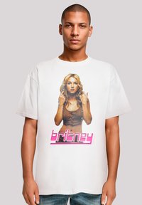 Weißes Baumwoll-T-Shirt mit einem Grafikmotiv einer Frau mit langen Haaren, die ein braunes Oberteil trägt, und dem Namen "britney" in pinker Schrift darunter.