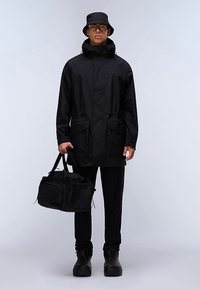 Czarna wodoodporna kurtka z kapturem, dwoma przednimi kieszeniami i sznurkiem w talii. W połączeniu z czarnymi spodniami, kapeluszem typu bucket i czarną torbą.