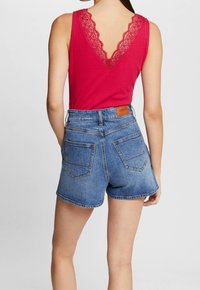 Rød ribbet tanktop med en blonde v-udskæring, parret med blå højtaljede denimshorts med to baglommer og et lædermærke.