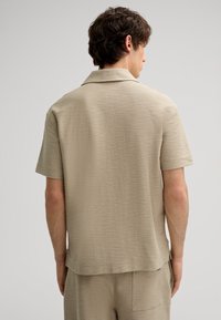 Beige Kurzarmhemd mit strukturiertem Finish und klassischem Kragen. Es hat einen geraden Saum und subtile Nähedetails.