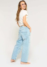 Lichtblauwe denim brede denimbroek met patchdetails en achterzakken, gecombineerd met een witte cropped t-shirt en paarse zonnebril.