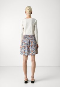 Blusa blanca de manga larga combinada con una falda estampada que presenta diseños en azul, naranja y flores, con una cintura fruncida y un dobladillo acampanado.