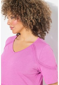 Top de pico rosa hecho de una tela suave, con detalles de tejido en los hombros y mangas cortas, con un corte relajado y textura suave.