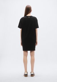 Čierne bavlnené šaty v štýle trička s voľným strihom, krátkymi rukávmi a dĺžkou po polovicu stehien. Na zadnej strane pri výstrihu je jemné logo.
