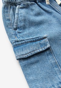 Shorts en denim de couleur bleu clair, avec un ourlet retourné, poches latérales et des coutures oranges contrastées. Texture douce, design décontracté.