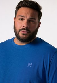 Camiseta azul de cuello redondo hecha de tejido suave. Presenta un pequeño logotipo en relieve en el lado izquierdo del pecho. Textura lisa con un ajuste relajado.