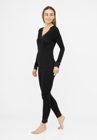 Haut noir à manches longues avec encolure en dentelle, associé à des leggings noirs avec des poignets en dentelle, texture lisse, coupe ajustée.