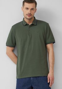 Donkergroen polo met marineblauwe kraagaccenten, twee knopen bij de hals, korte mouwen en een subtiele geborduurde logo op de borst.