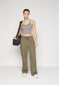 Top cropped atlético cinza com detalhes em verde limão, combinado com calças de moletom verde-oliva com bolsos tipo cargo. Modelo carrega uma mala de desporto preta.