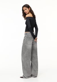 Sort off-the-shoulder langærmet top parret med højtsiddende, løs grå denim jeans med baglommer og en falmet finish.