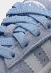 Κοντινή λήψη ανοιχτόμπλε αθλητικού παπουτσιού, με υφασμάτινο επάνω μέρος με υφή, επίπεδα κορδόνια και λευκή λαστιχένια σόλα με ζιγκ-ζαγκ διακοσμήσεις.