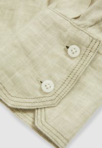 Helles beiges Leinengewebe mit einem Doppelknopfverschluss, gesteppten Details und einer strukturierten Optik.