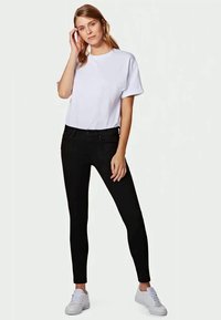 Camiseta blanca de manga corta combinada con vaqueros ajustados negros, con una textura suave y un diseño ajustado, y llevada con zapatillas blancas.