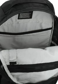 Schwarzer Rucksack innen mit grauem Futter, ausgestattet mit Aufbewahrungstaschen und einem Reißverschluss. Sichtbares Etikett mit Produktdetails und Anweisungen.