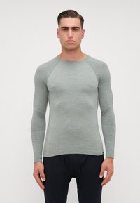Camisa justa de manga longa em verde claro, feita de tecido de malha texturizada. Apresenta mangas raglan e um decote redondo com punhos canelados.