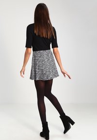 Haut noir à manches courtes associé à une jupe patineuse grise à motifs. La jupe présente des rayures verticales et une coupe évasée. Bottines noires.