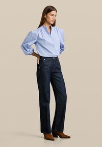 Blauw-wit gestreepte blouse met puffmouwen, gecombineerd met donkere denim hoge taille jeans. Bruine laarzen met hak maken de outfit compleet.