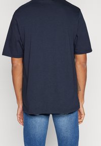 Granatowa bawełniana koszulka z luźnym krojem, krótkimi rękawami i prostym dołem; gładka struktura bez grafik i akcentów.