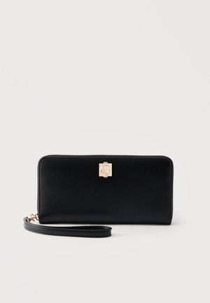 Czarny skórzany portfel na nadgarstek ze złotym zapięciem i odpinanym paskiem na białym tle.