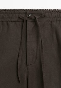Pantaloni in lino marrone scuro con vita elasticizzata, cintura in tessuto e un unico bottone visibile al centro davanti.