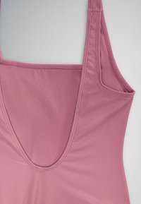 Close-up of a sleeveless pink ribbed tank top with a deep scoop neckline and wide shoulder straps on a light background.