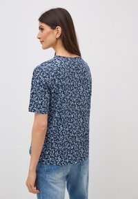 Camiseta de color navy con un estampado de hojas en azul claro, de manga corta y cuello redondo. Combinada con jeans de mezclilla claros.