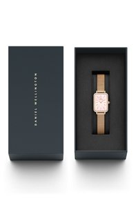 Reloj rectangular en oro rosa con correa de malla, presentado en una caja azul oscura con texto de la marca en dorado y un interior de terciopelo negro.