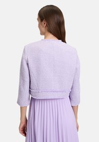 Liliowa kurtka typu cropped z teksturowanej, tkanej tkaniny, z rękawami do łokcia i surowym wykończeniem, noszona na dopasowanej, plisowanej sukience.