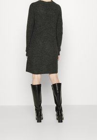 Abito in maglia in lana grigia scura, maniche lunghe, lunghezza al ginocchio, con scollatura arrotondata. Abbinato a stivali neri a ginocchio con motivo coccodrillo.