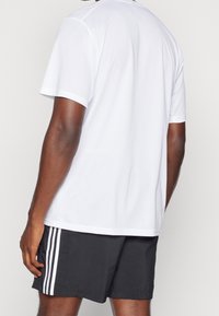 Camiseta atlética de manga corta blanca con una tela texturizada, combinada con pantalones cortos negros que presentan tres rayas verticales blancas en el costado.