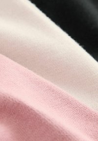 Mangefarvet stof med tre vandret striber: sort, creme og lys pink. Teksturen er blød og lidt struktureret.
