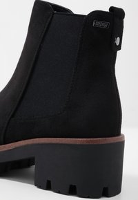 Černé kotníkové boty s semišovým svrškem a elastickými bočními panely, černou gumovou podrážkou a hnědým akcentem na mezipodešvi.