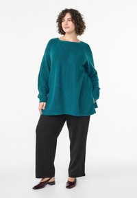 Teal oversized sweater with textured knit, wide neckline, and long sleeves, paired with black wide-leg trousers and dark heeled shoes.