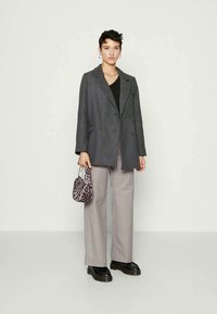Young person wearing gray double-breasted blazer, black top, beige pinstriped pants, black platform shoes, and holding a small leopard print handbag.