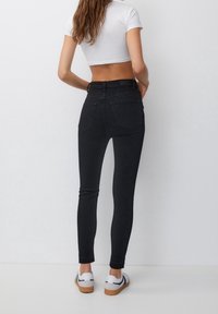 Jean noirs taille haute avec une coupe slim, dotés de poches arrière et d'une texture denim lisse. Assortis avec des baskets blanches.