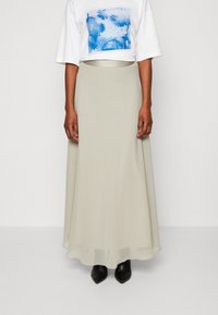 Lång, flödande ljusbeige kjol i mjukt tyg, tillsammans med en vit t-shirt med grafiskt tryck som har blå blommönster. Svarta klackstövlar.